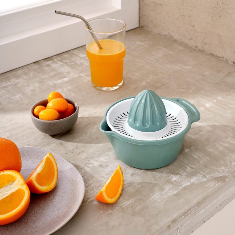 Presse-agrumes turquoise avec des oranges et un verre de jus d'orange.